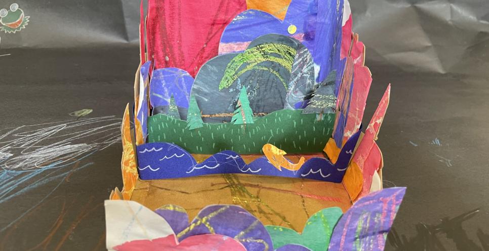 Colorful paper collage tunnel box. There is a paper river with a fish jumping and trees in the background.