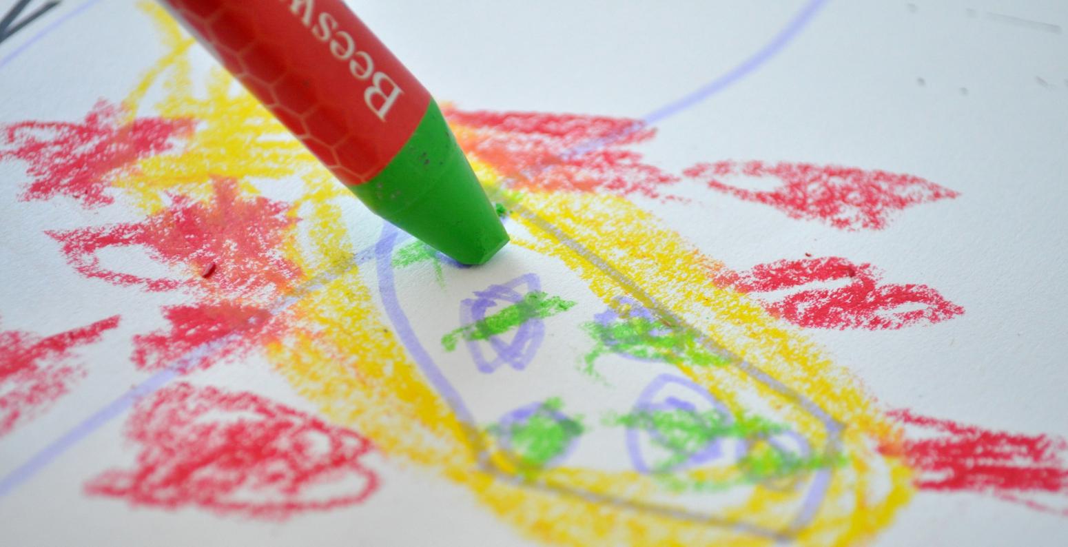 Green pastel crayon making marks on colorful piece of paper