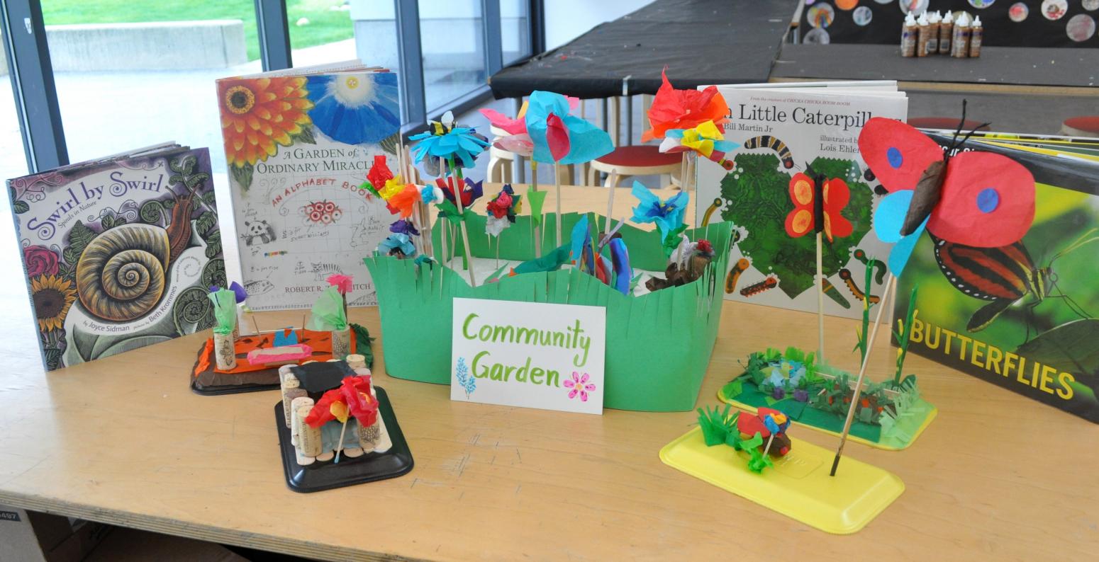 A community garden sculpture made of tissue paper collages with a backdrop of picture books about nature.