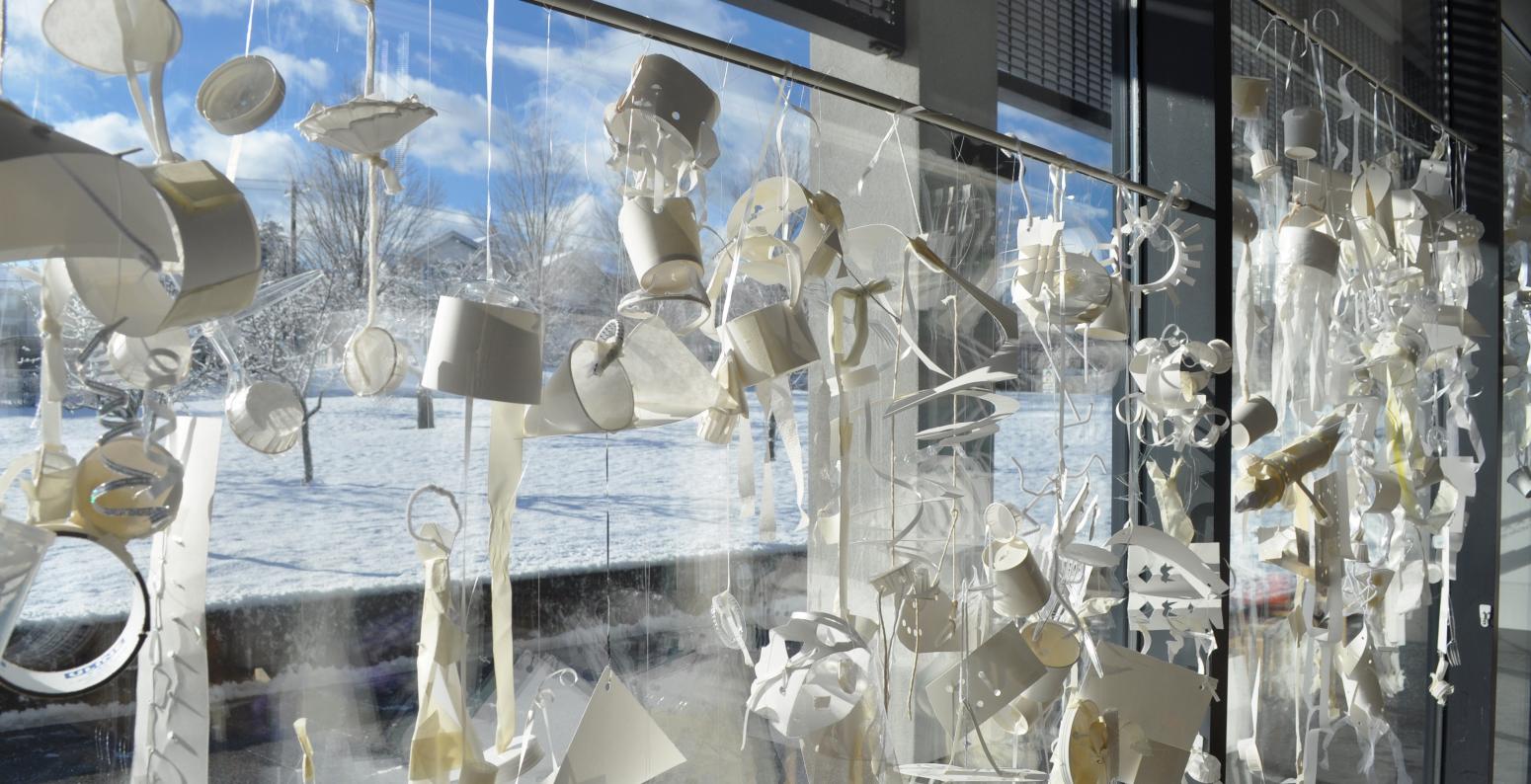 A window filled with white mobiles with a snowy day outside.