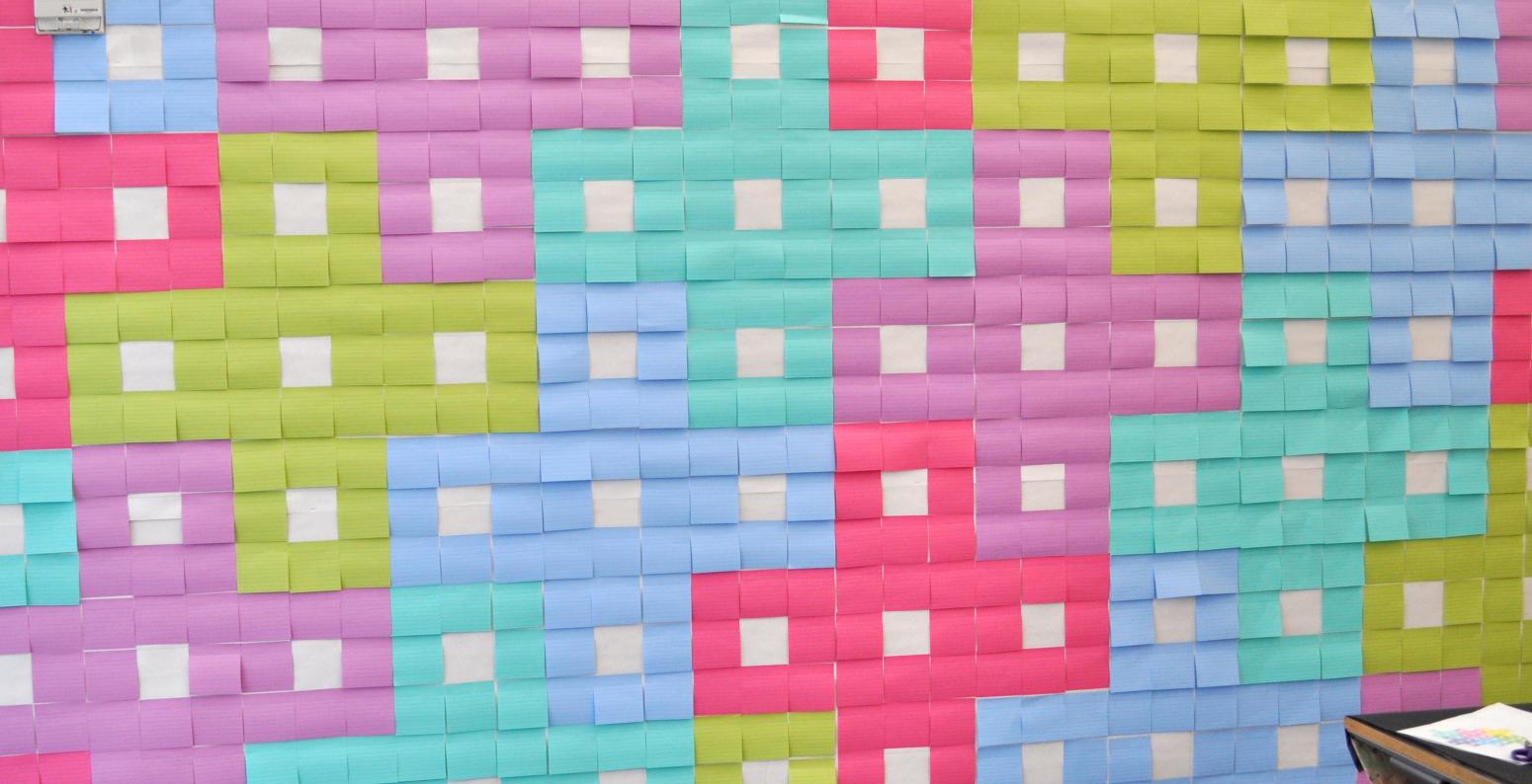 A wall covered in blank, colorful sticky notes creating a pattern.