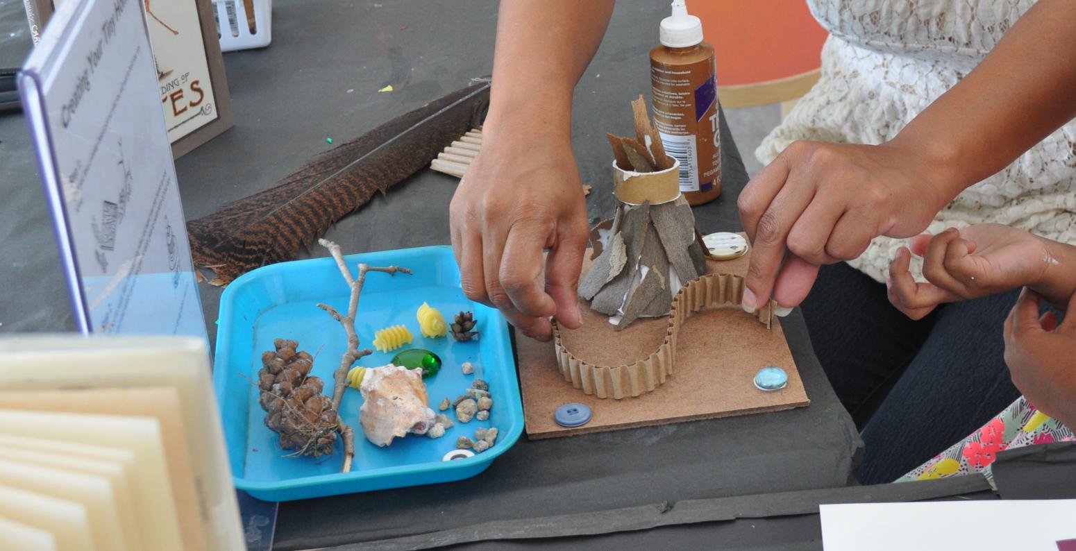 An adult and child working together to make a home made out of natural materials and cardboard.
