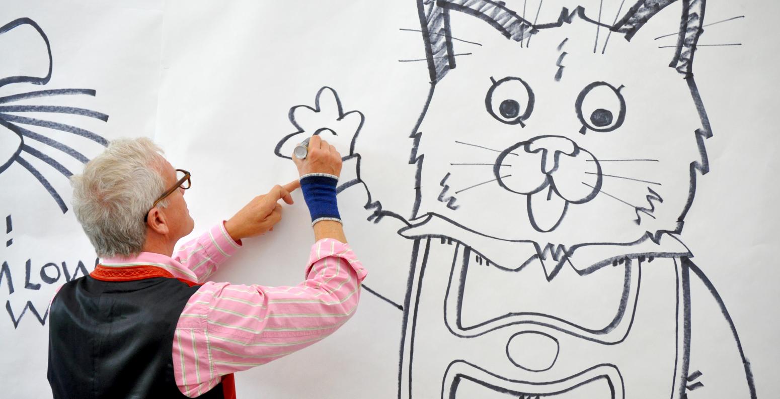 Author/illustrator Huck Scarry drawing a large character on a white wall in black Sharpie.