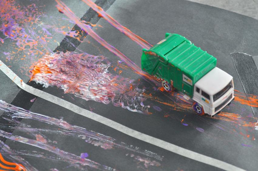 A toy truck with paint on its wheels runs across a black piece of paper.
