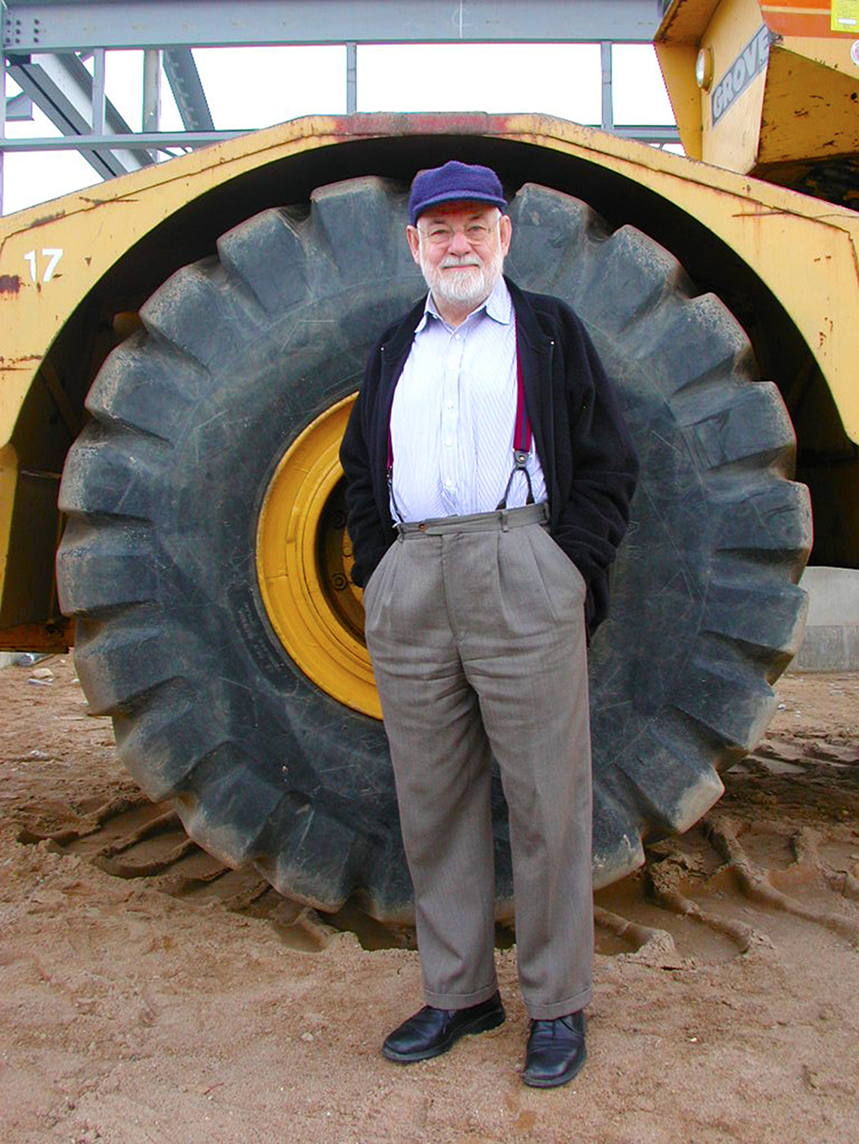 Eric Carle infront of a large construction vehicle wheel, which is as tall as he is