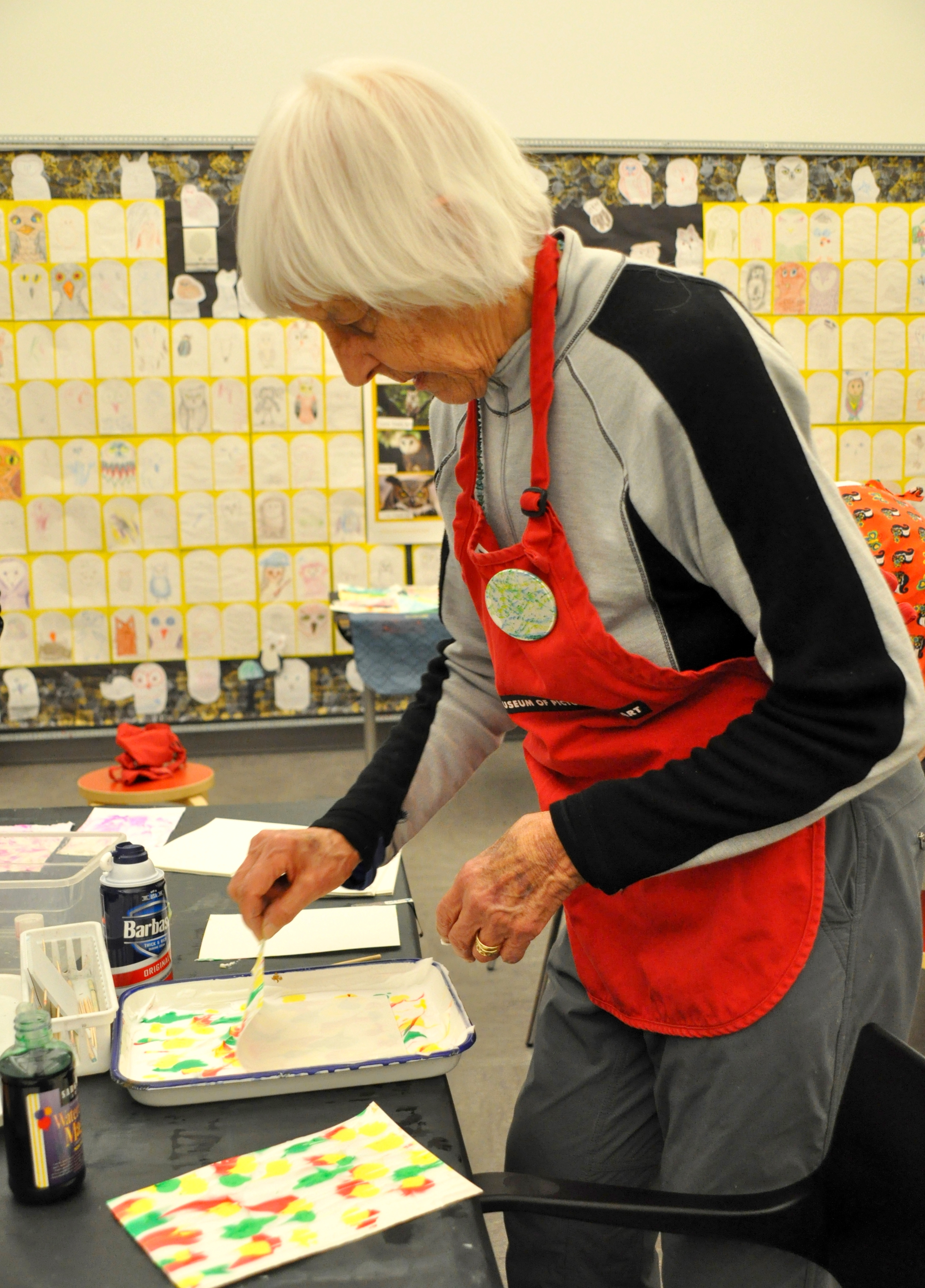 A woman pulls paper off of a tray of colored shaving cream to reveal a marbled paper.