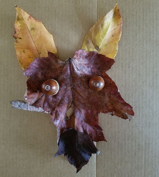 Collage of a fox face made with a variety of brown leaves and acorns for eyes.