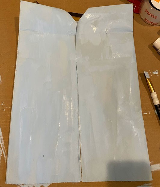 the paper bag has been cut into the shape of a vest and painted with pale blue paint.