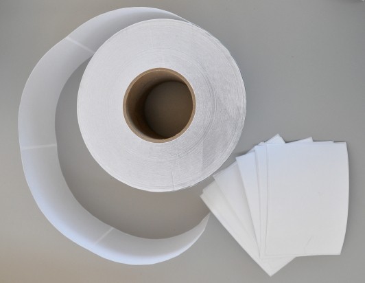 A roll of white labels and a stack of individual labels next to the roll