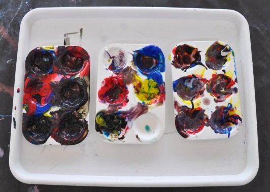 Three paint palettes covered in paint on a white tray.
