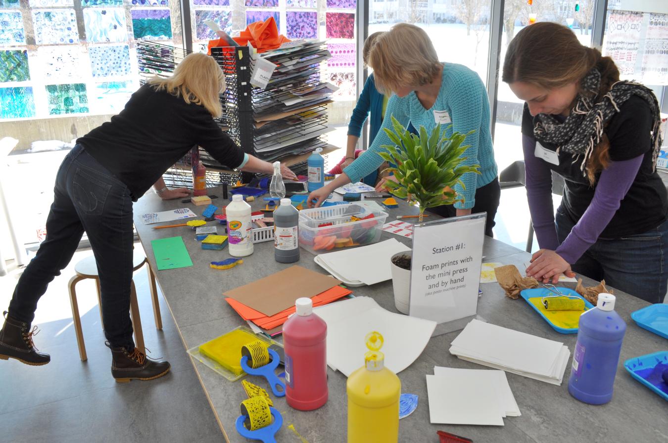 Adults standing at a table and hand printing with tempera paint.