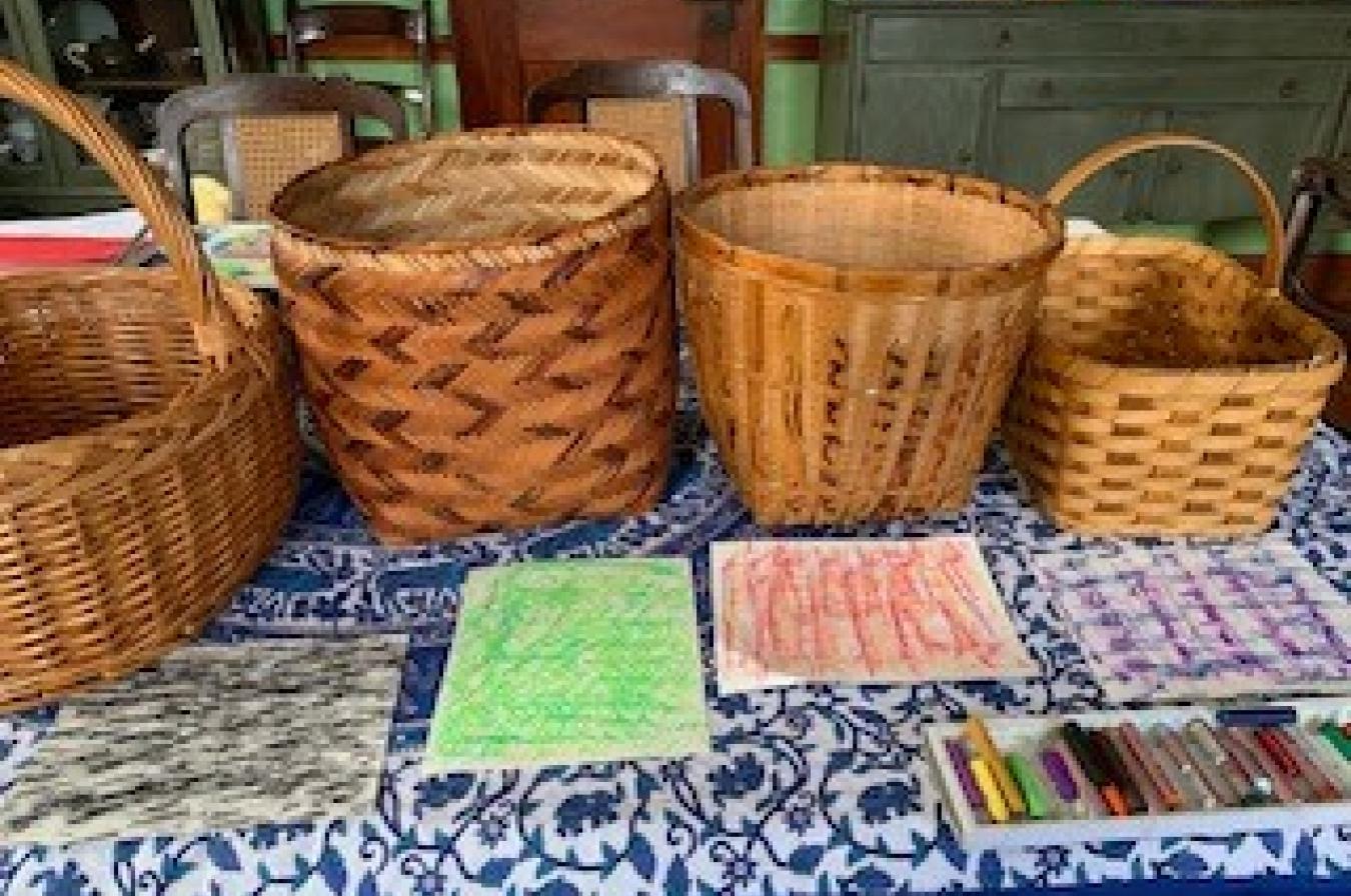 A line-up of four wicker baskets with papers laid in front of them. Each paper was a different rubbing made from the baskets.