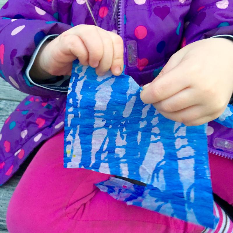 A young child tearing a piece of watercolor-painted paper.