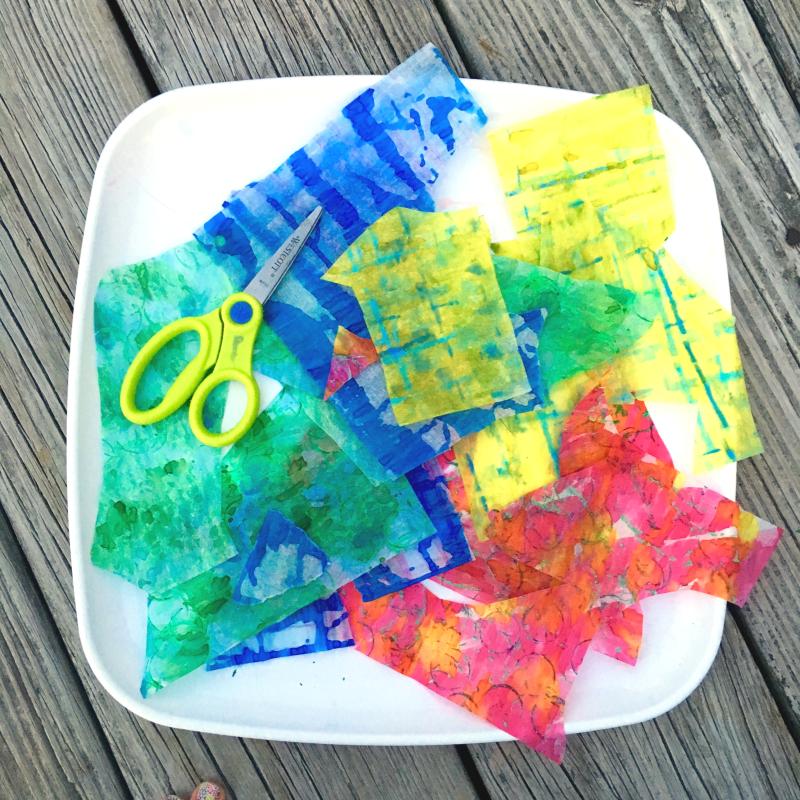 A tray with pieces of watercolor-painted papers and a pair of scissors.