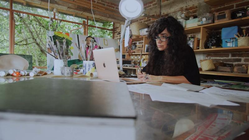Children’s book author and illustrator Yuyi Morales works on her latest picture book at her desk while surrounded with sketches, paints, and art supplies.