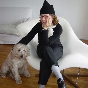 Maira Kalman sitting in white chair with white terrier dog, Pete. 