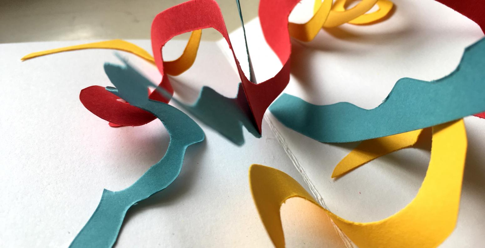 Red, yellow, and blue paper swirls popping up out of a hand-made book