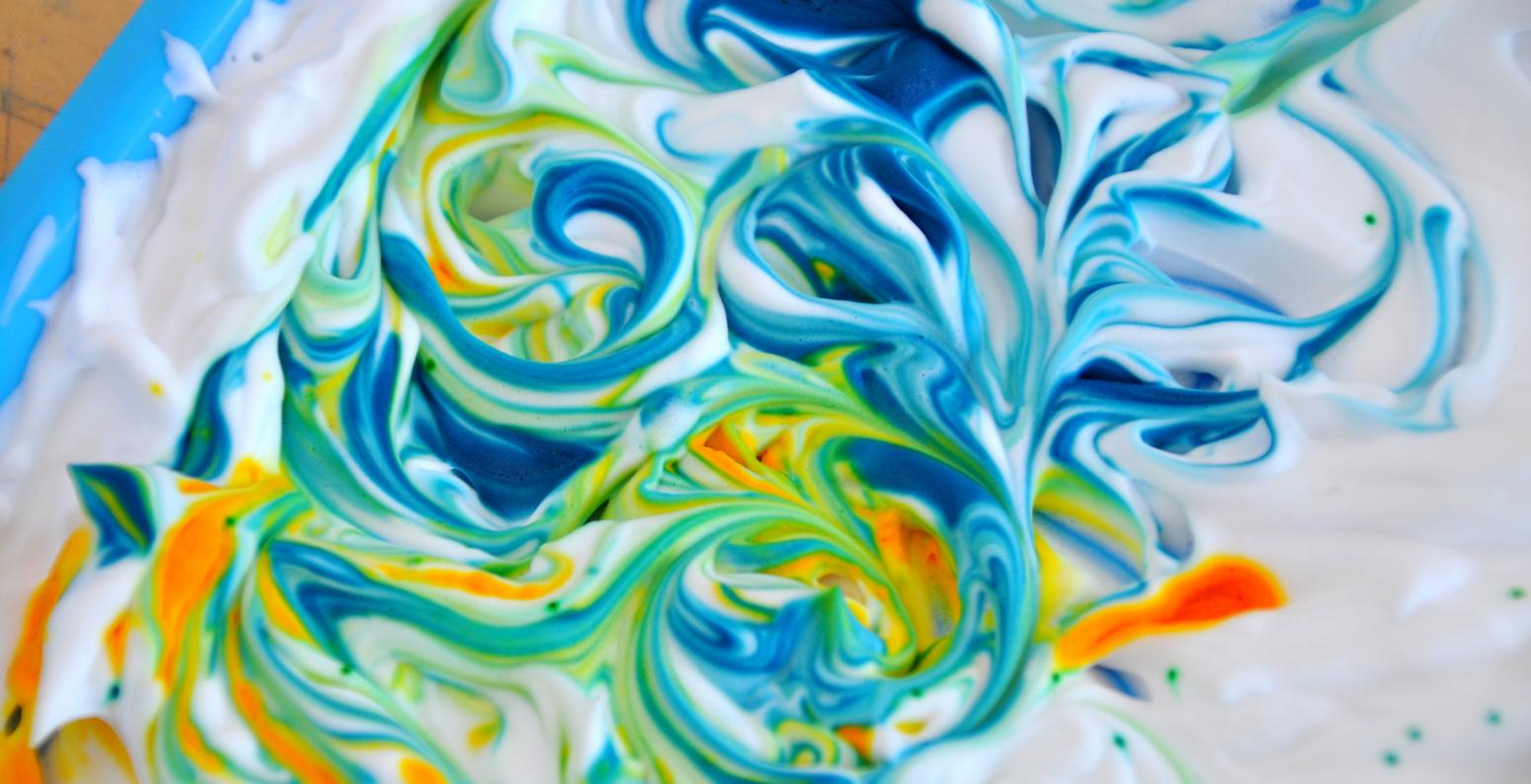 Blue and yellow swirls of color within white shaving cream.