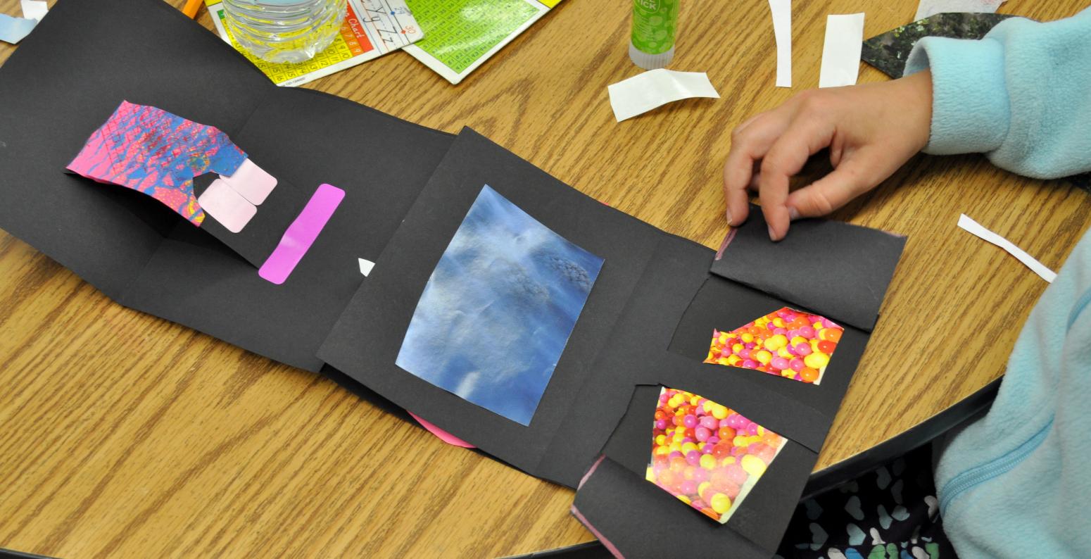 A child pulling back lift flaps on their black accordion fold book to reveal colorful red collage papers.