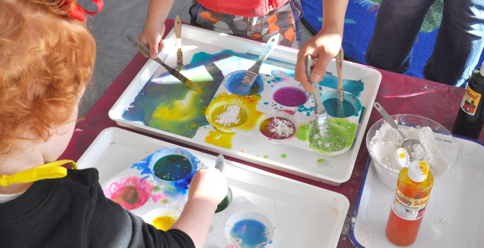 Young painters dipping brushes into colorful palettes.