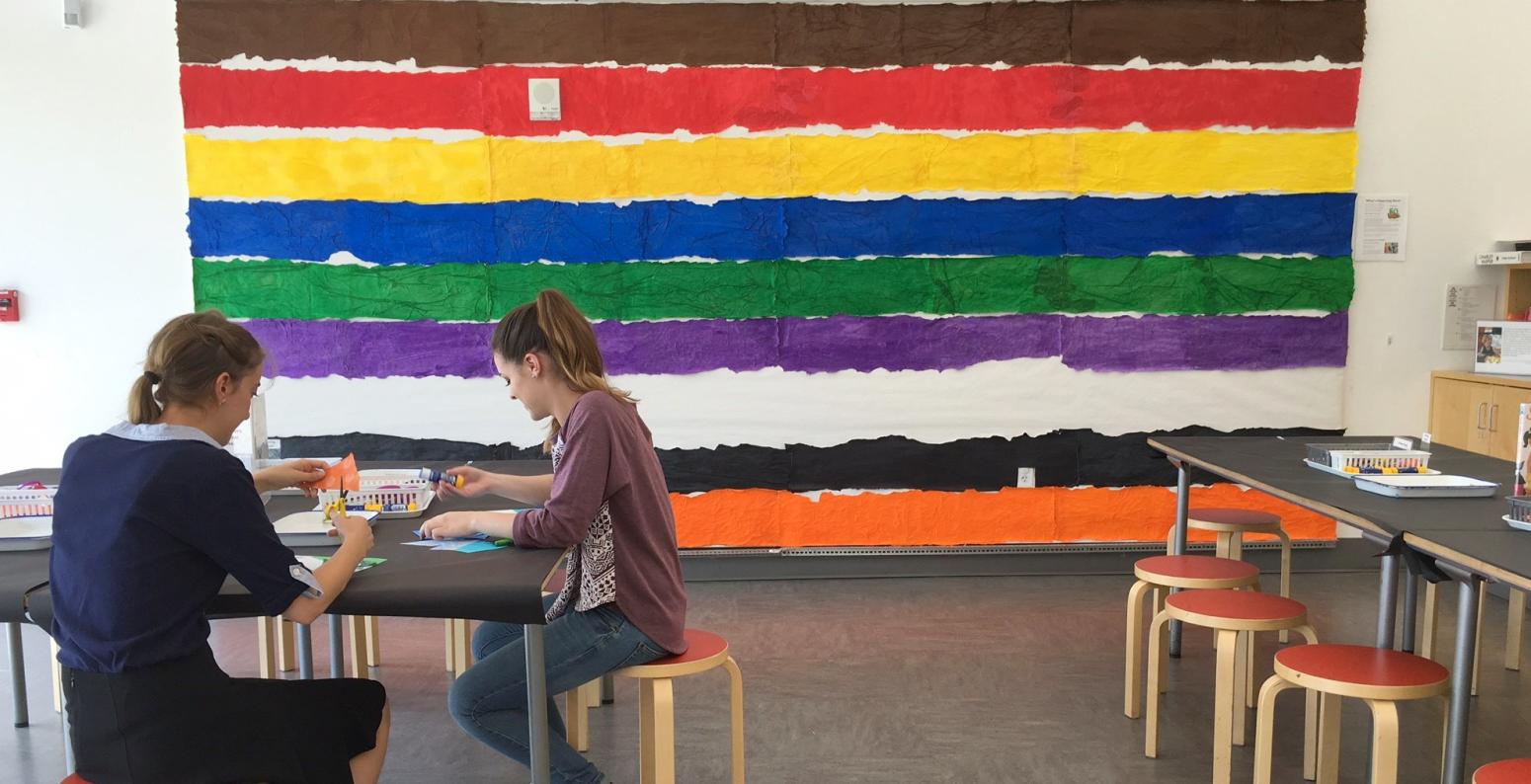 Two people sitting at an Art Studio table with the Brown Bear endpaper display wall behind them.