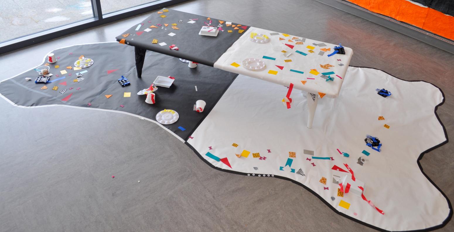 A table and floor covered in black and white paper with colorful stickers on it.