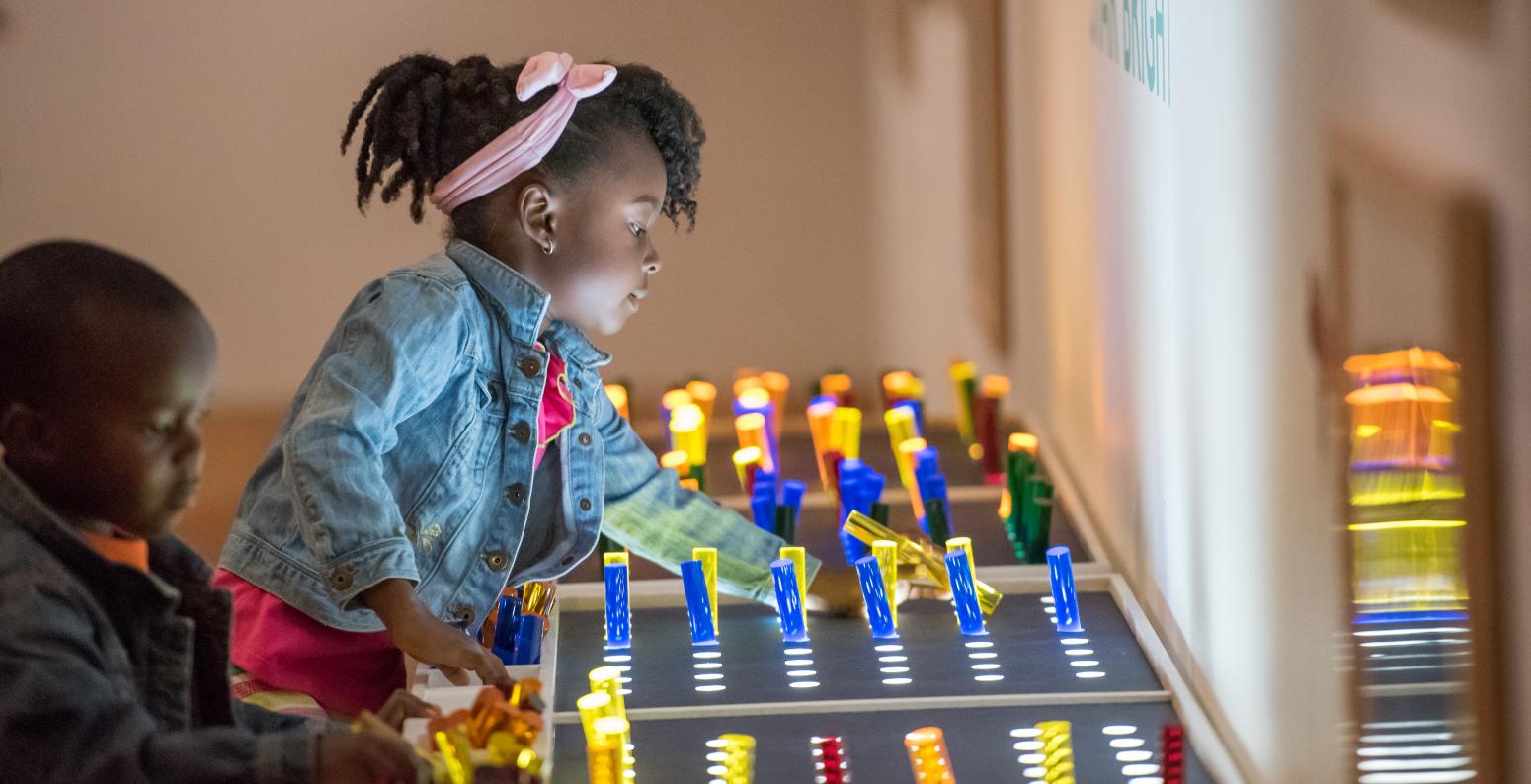 Two young children play with a light table and translucent color sticks.