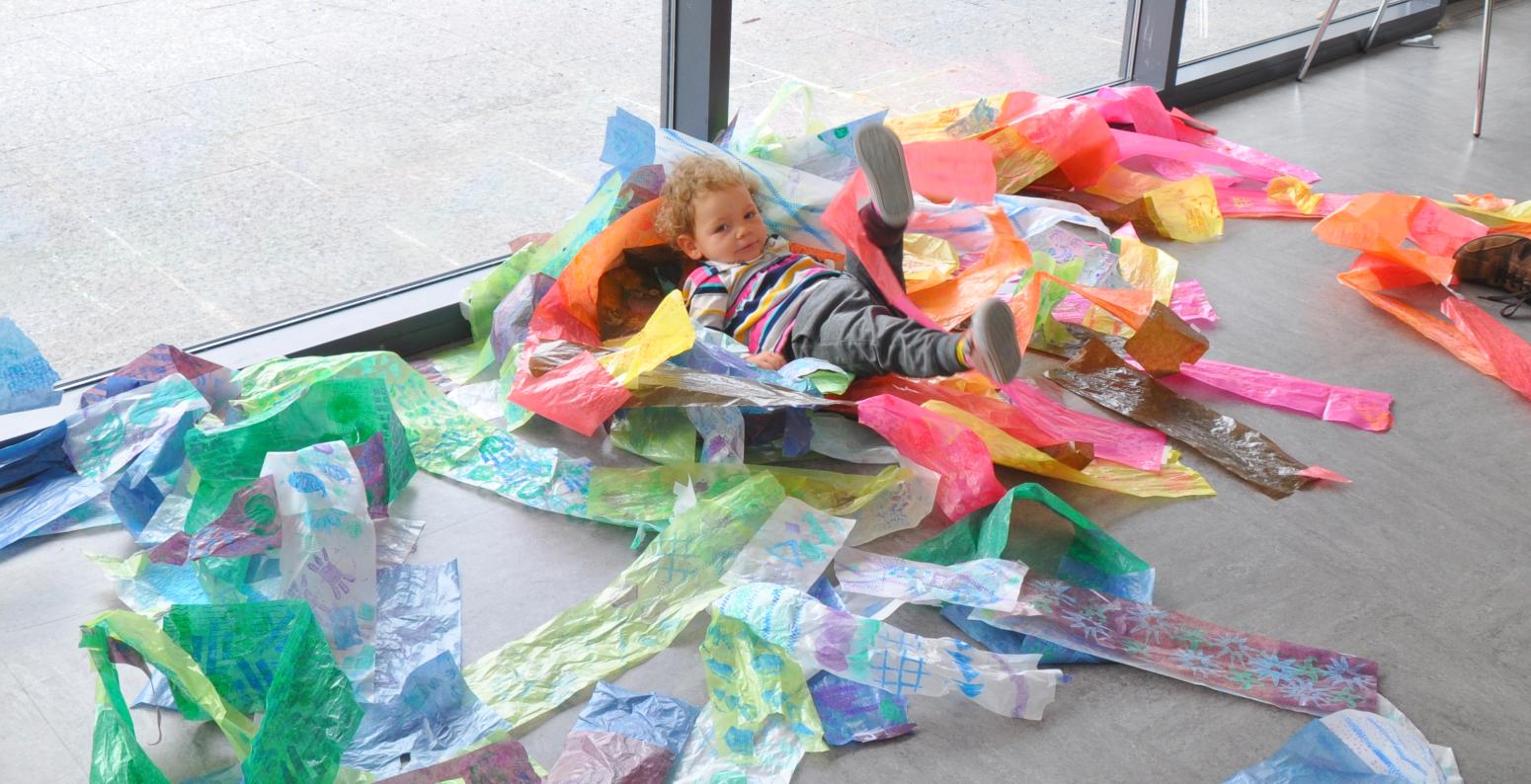 A young child playing within a pile of colorful papers on the ground.