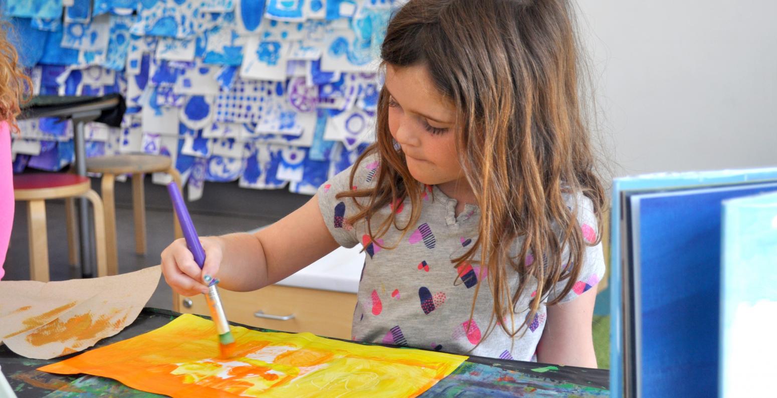 A child painting with orange and yellow paint onto a white piece of paper.