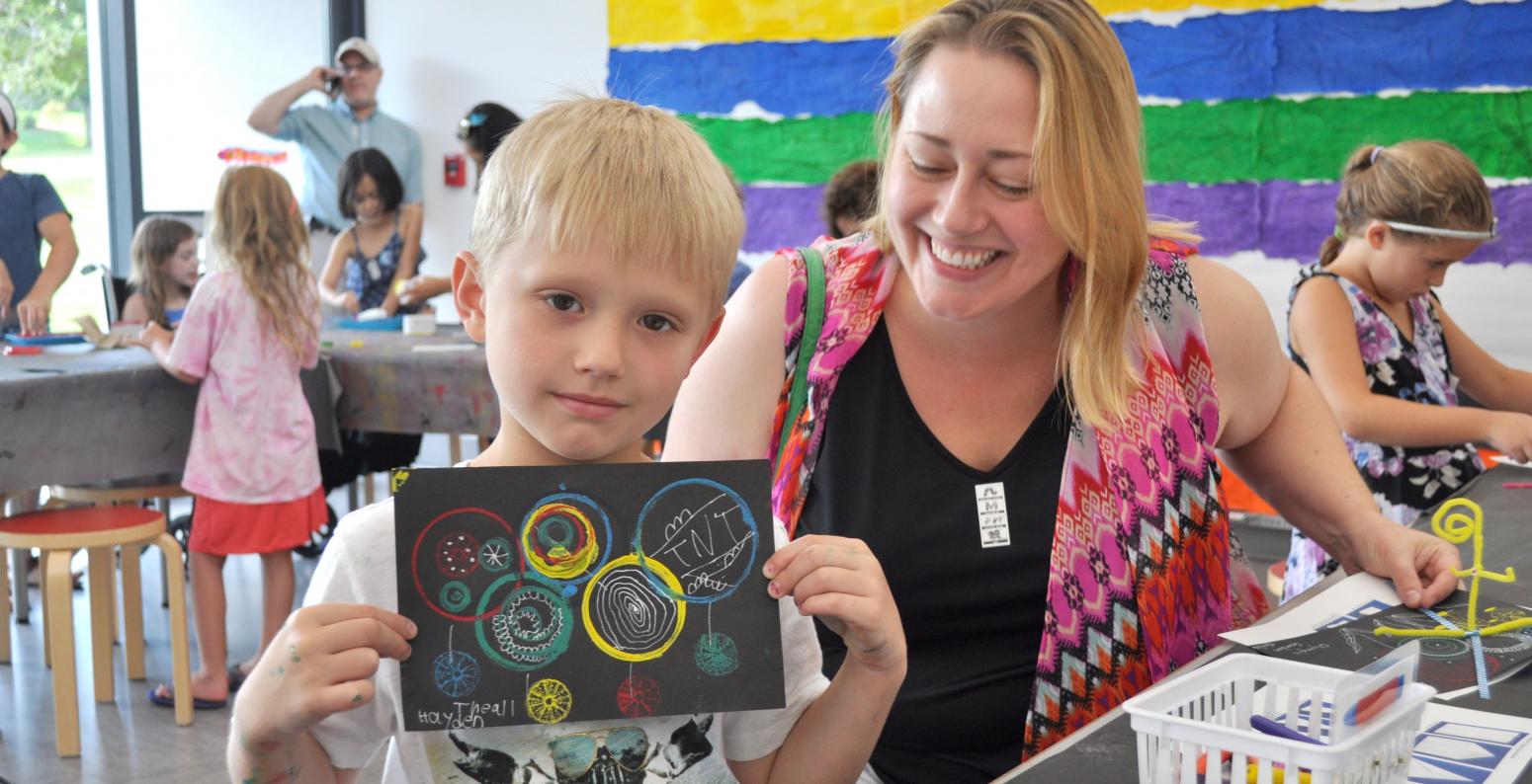 An adult and child smiling and holding up their circle-stamped paper.