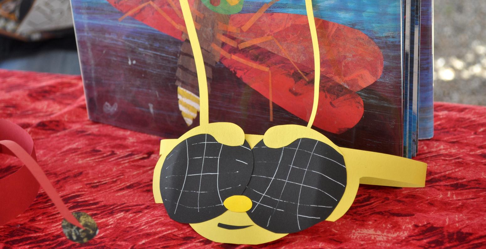 A paper hat that looks like the face of a bee in front of the picture book "The Very Lonely Firefly."