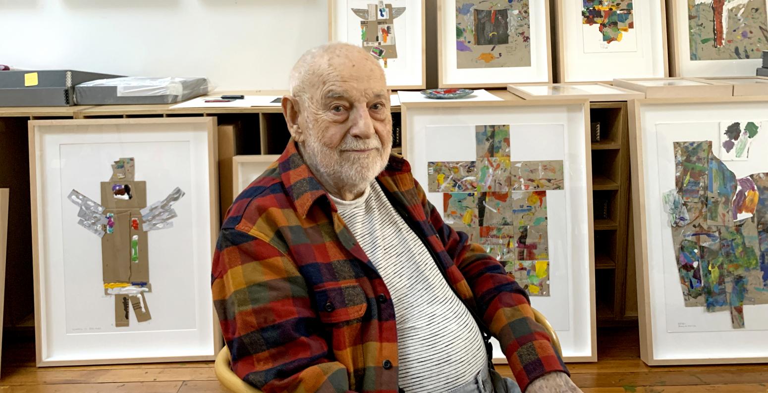 Eric Carle sitting in studio with framed Angels. 