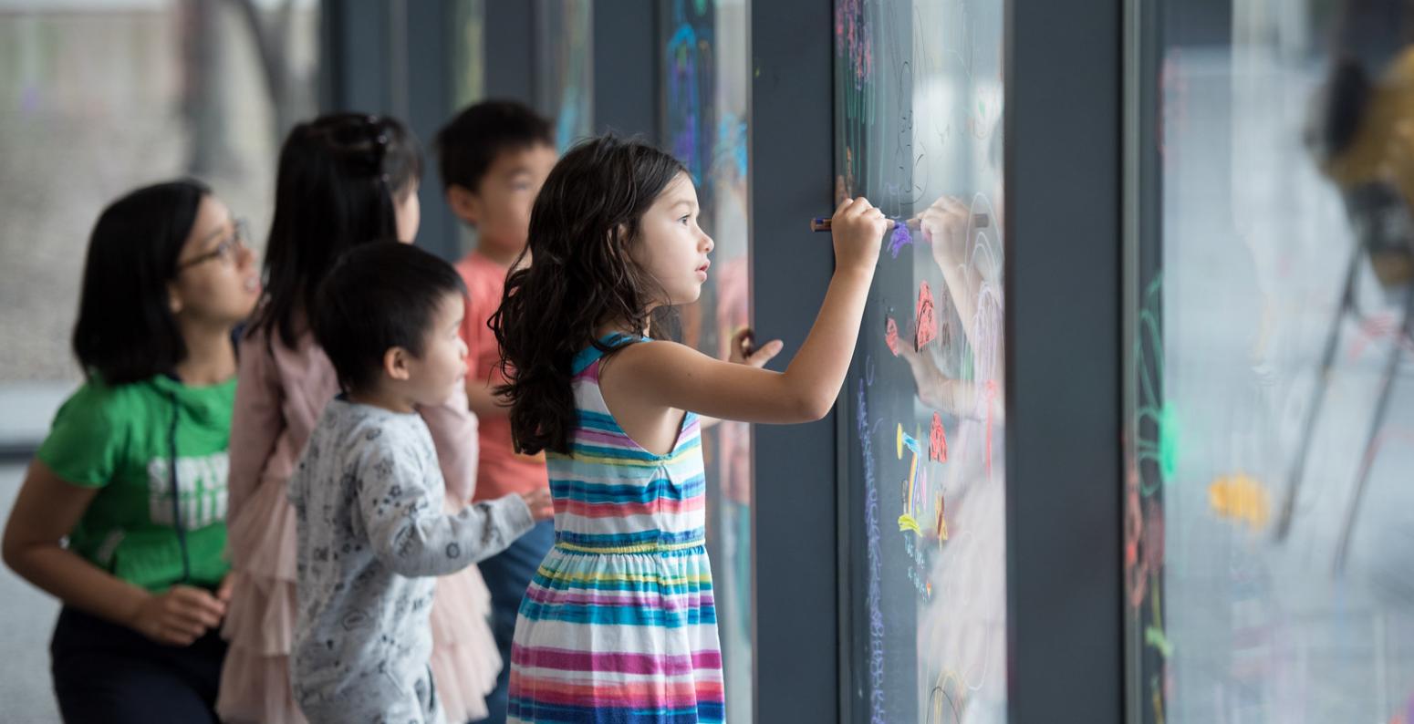Children writing with Stabilo watercolor pencils on a large window.