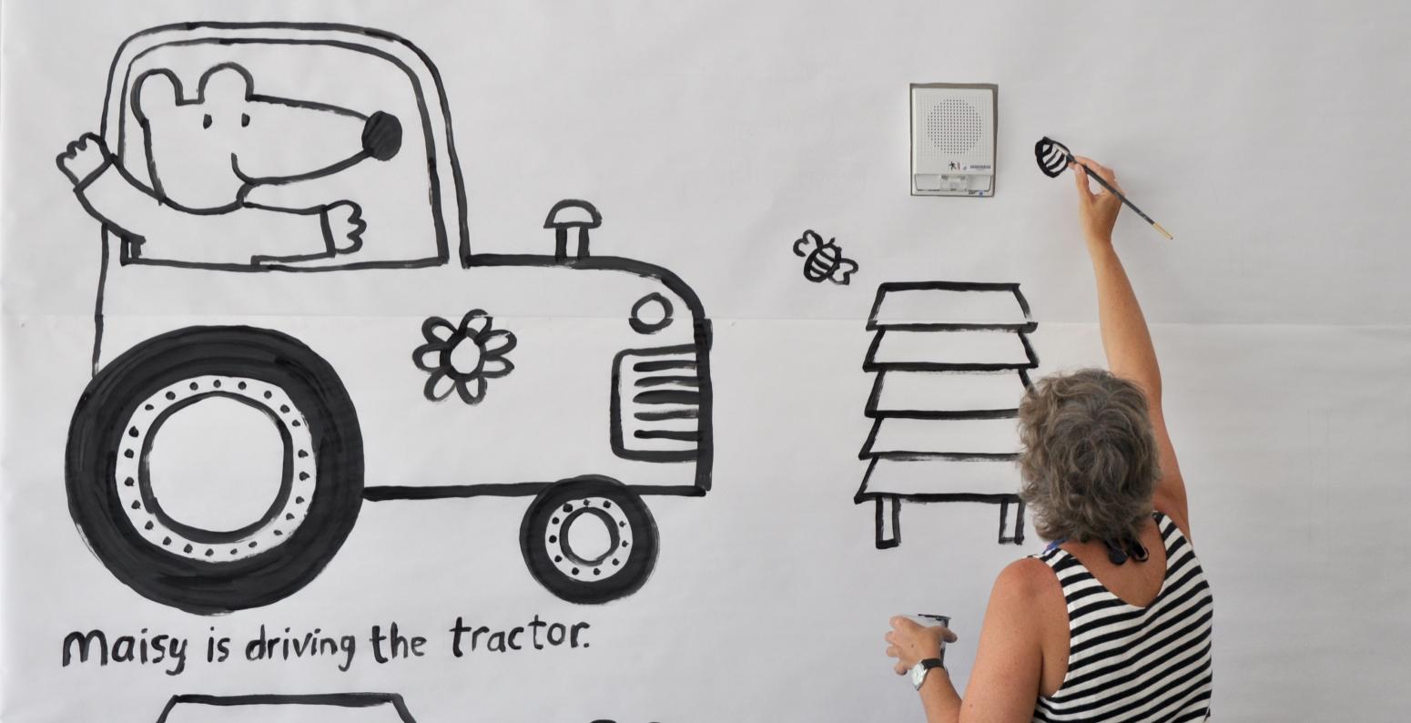 Author/illustrator Lucy Cousins painting a mural with black paint on a white wall.