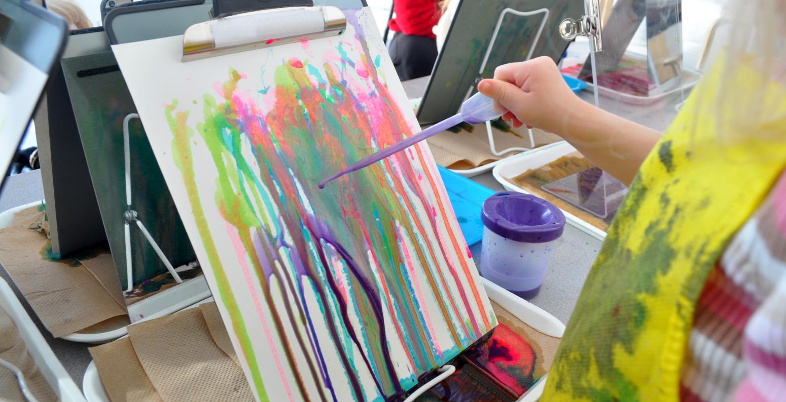 A toddler painting with a dropper and liquid watercolor onto a vertical piece of paper clipped into a clipboard.