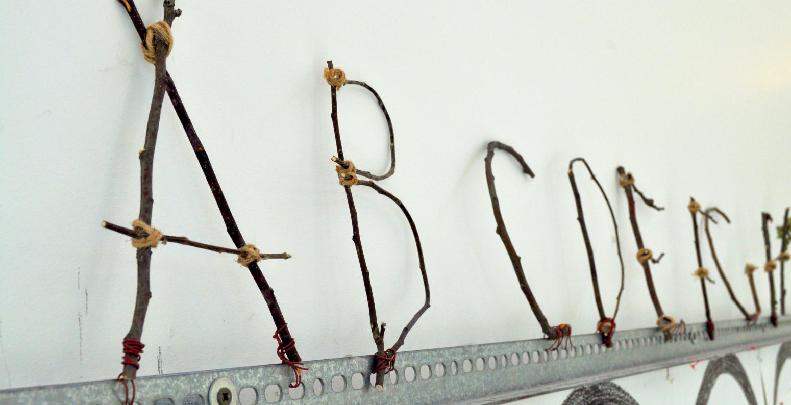 An alphabet made from twigs and twine attached to a long metal rail.