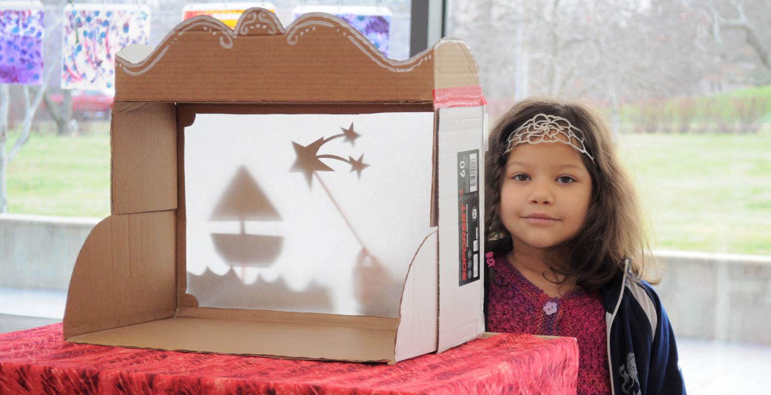 A child playing with a shadow puppet theater made from a copy paper box.