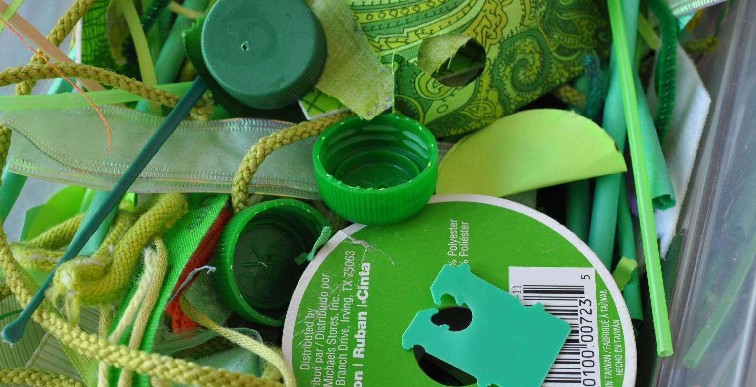 A collection of assorted green found materials including bread tabs, bottle caps, and yarns.