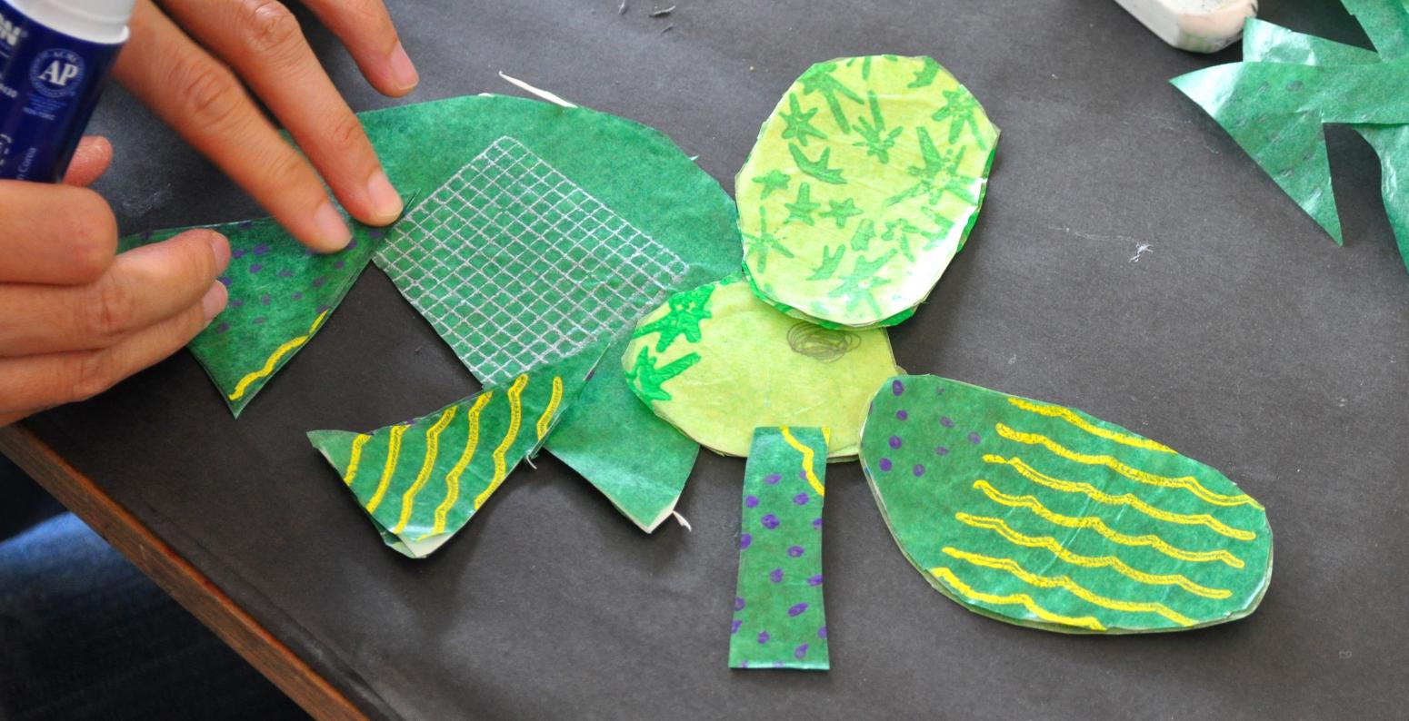A hand glues together a green elephant mobile.
