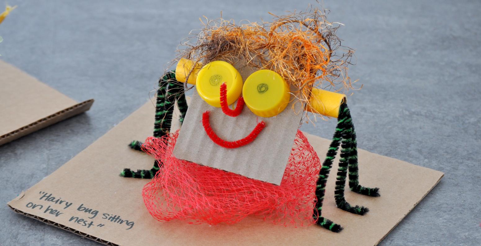 A smiling sculpture made of found materials with the title "Hairy bug sitting on her nest."