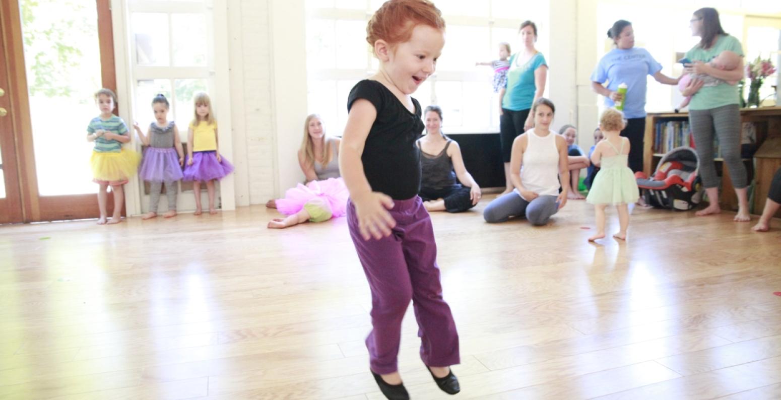 Word Play.jpg A young child jumps in the air as families watch in the background.