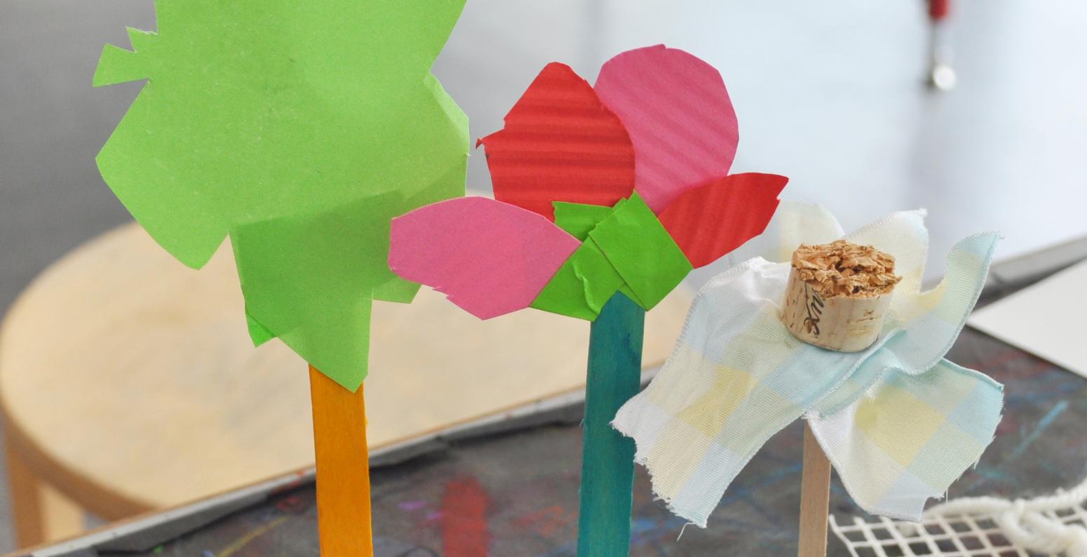 Three flower sculptures made from found materials including papers, corks, ribbons, and popsicle sticks.