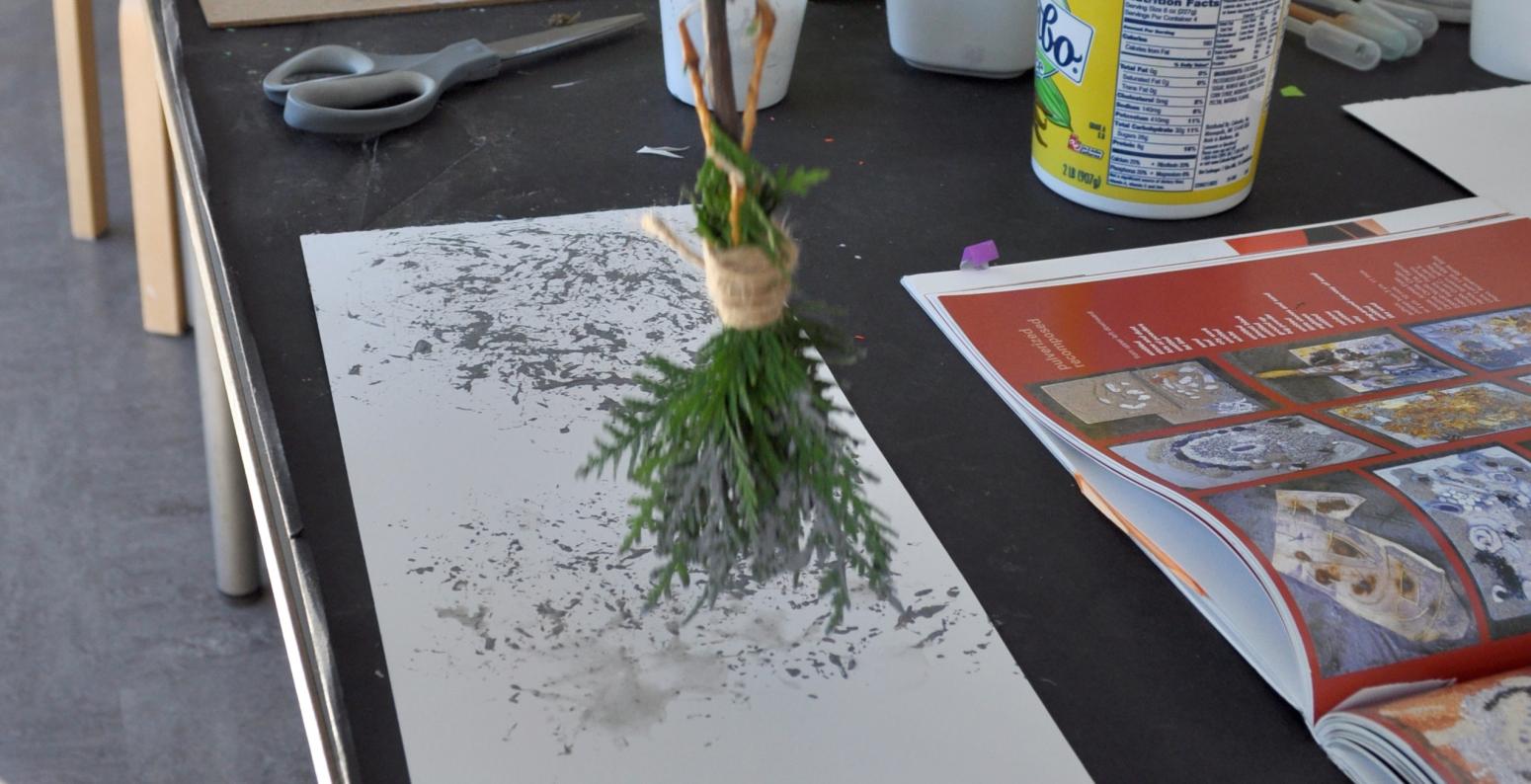 An adult painting with a clay and water mixture using a homemade paintbrush made from a twig and leaves.