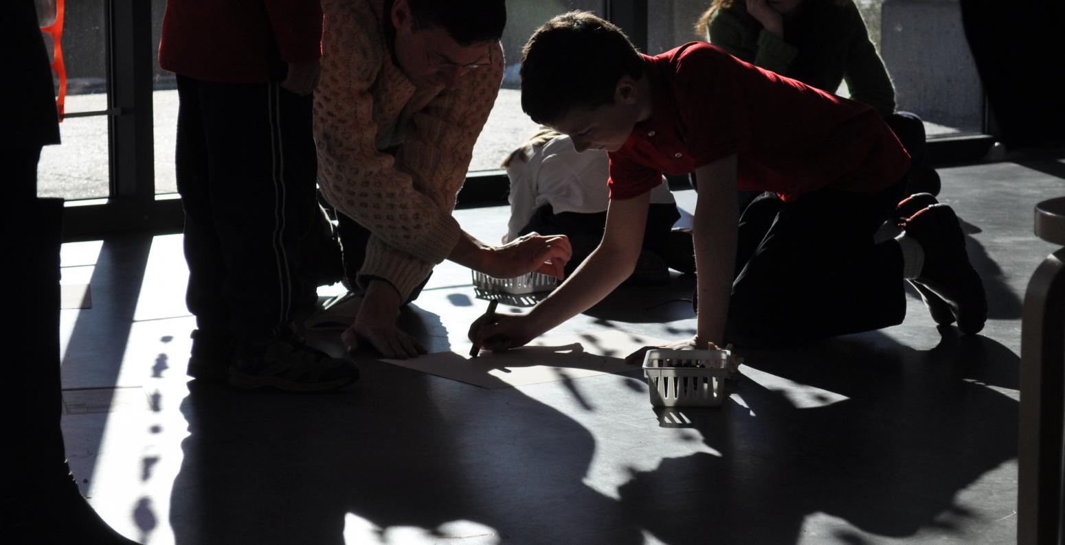A group of people using shadows to draw on paper attached to the ground.