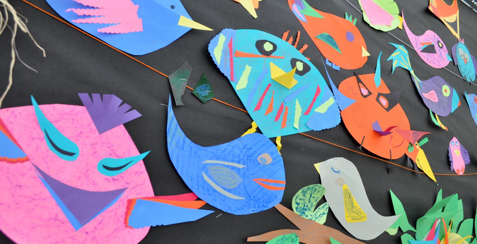 A flock of colorful paper bird collages on a black display wall.
