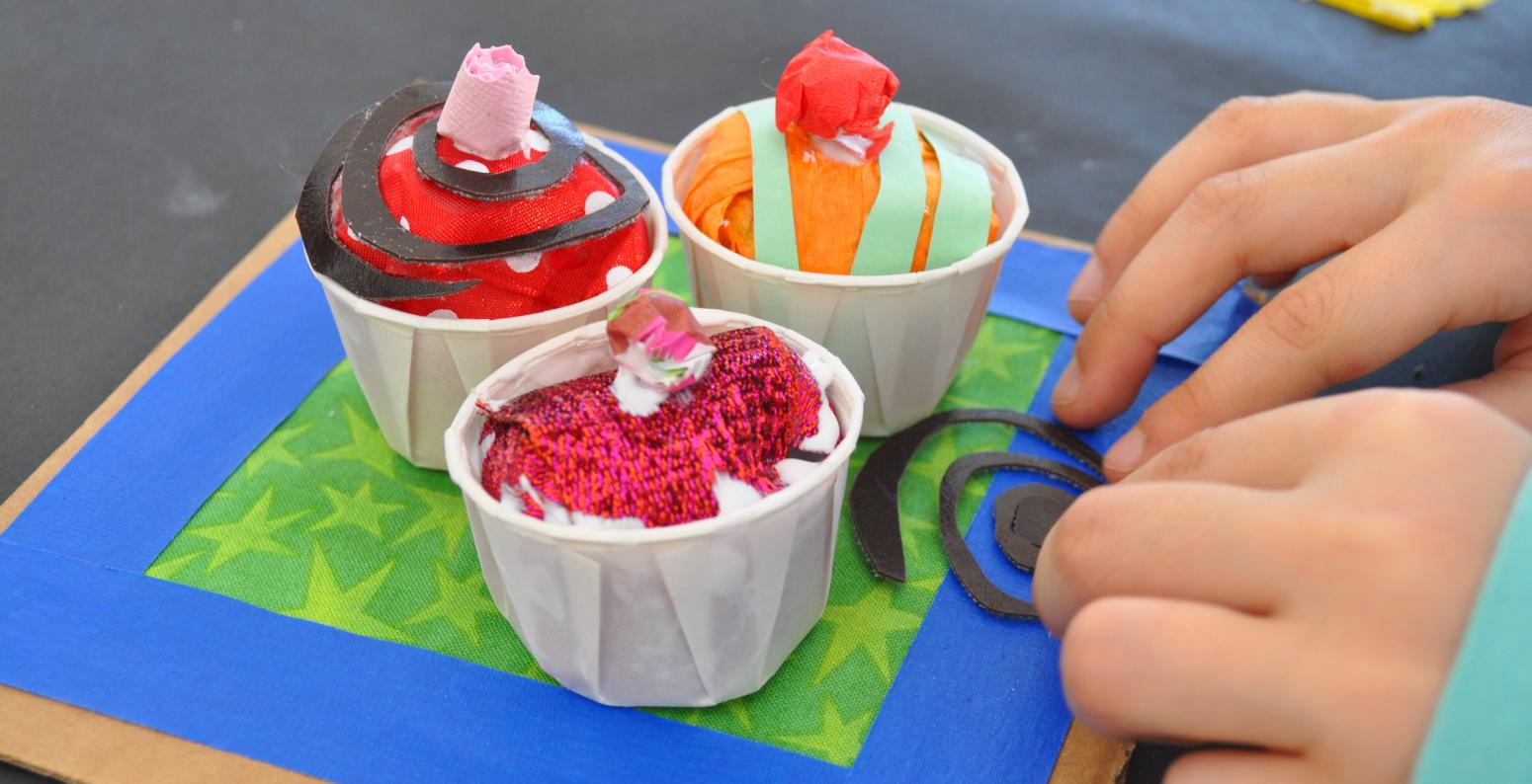 A young child places a spiral paper onto her found material sculptures of miniature cupcakes.