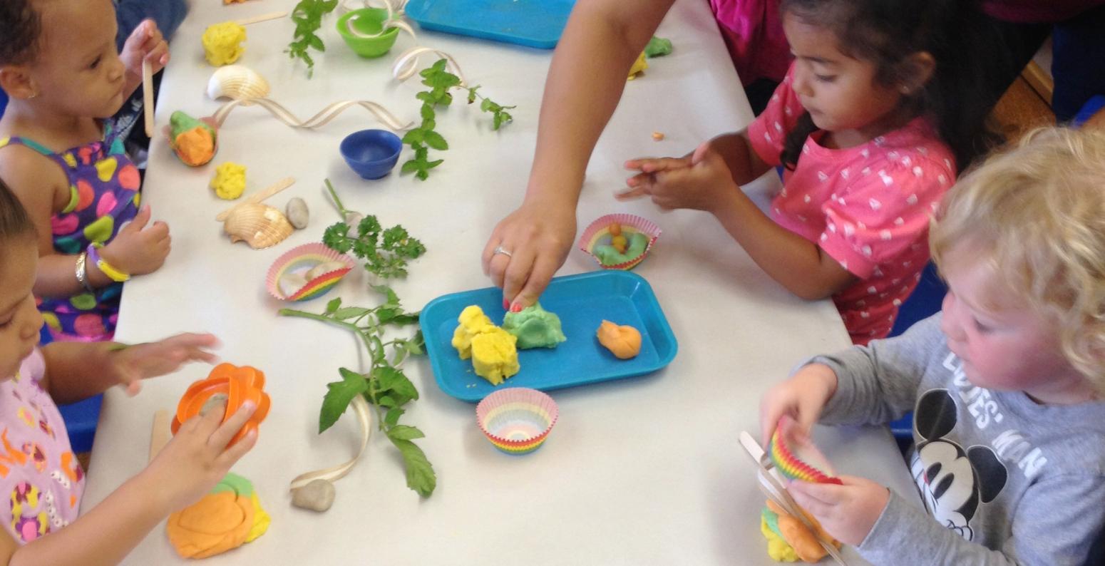 A group of toddlers playing with homemade dough and herbs at a table.