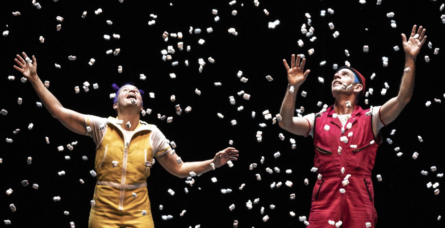 Two people on stage in front of a black background with white confetti