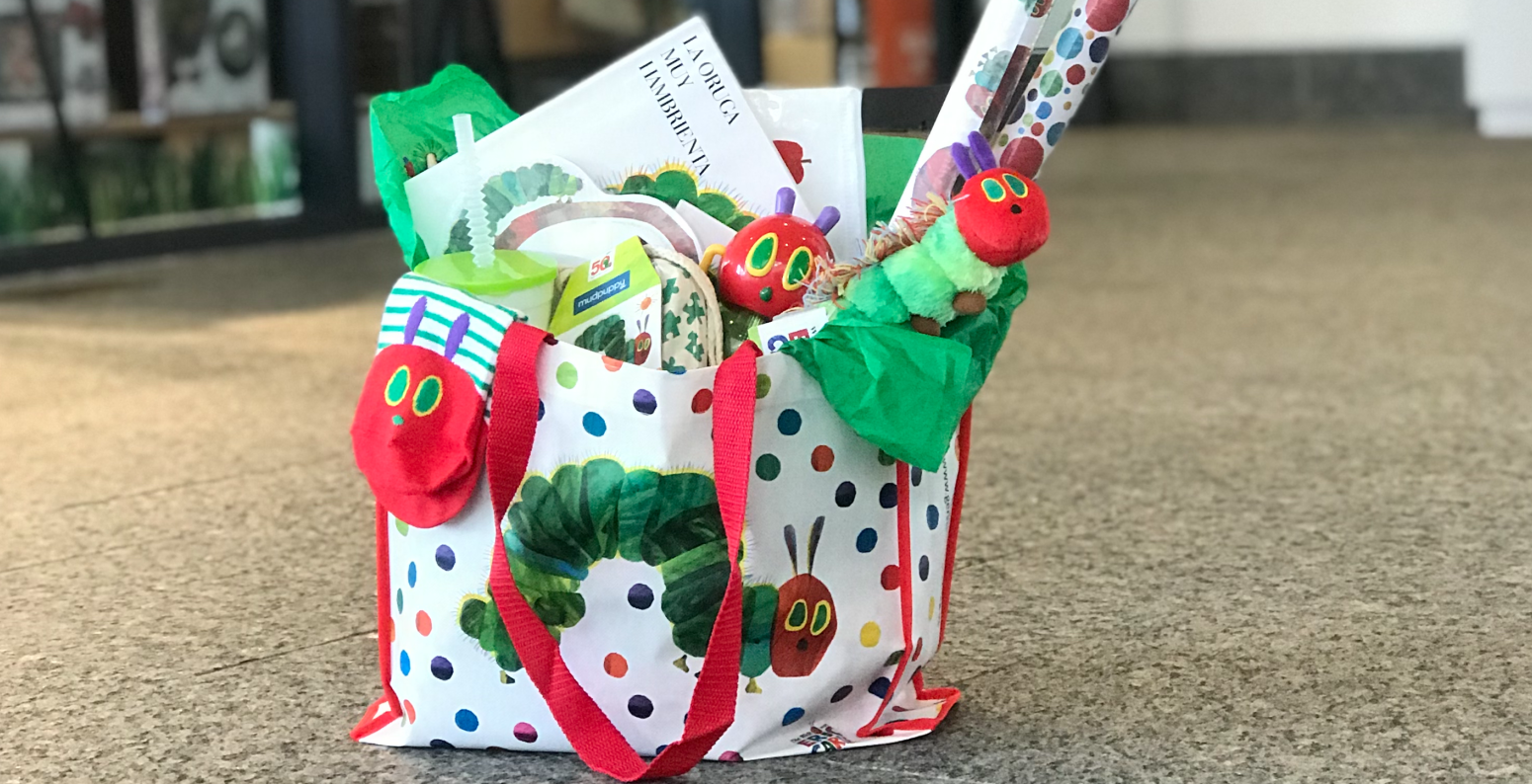 A Very Hungry Caterpillar tote bag filled with Caterpillar products is set on the floor in front of the museum shop.