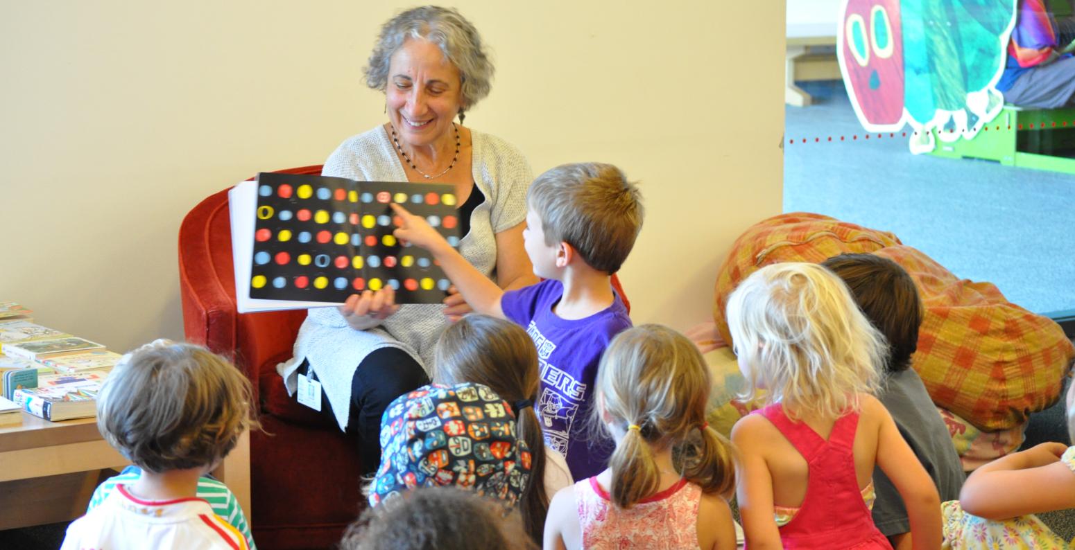 Group of children looking and pointing at book held by adult.